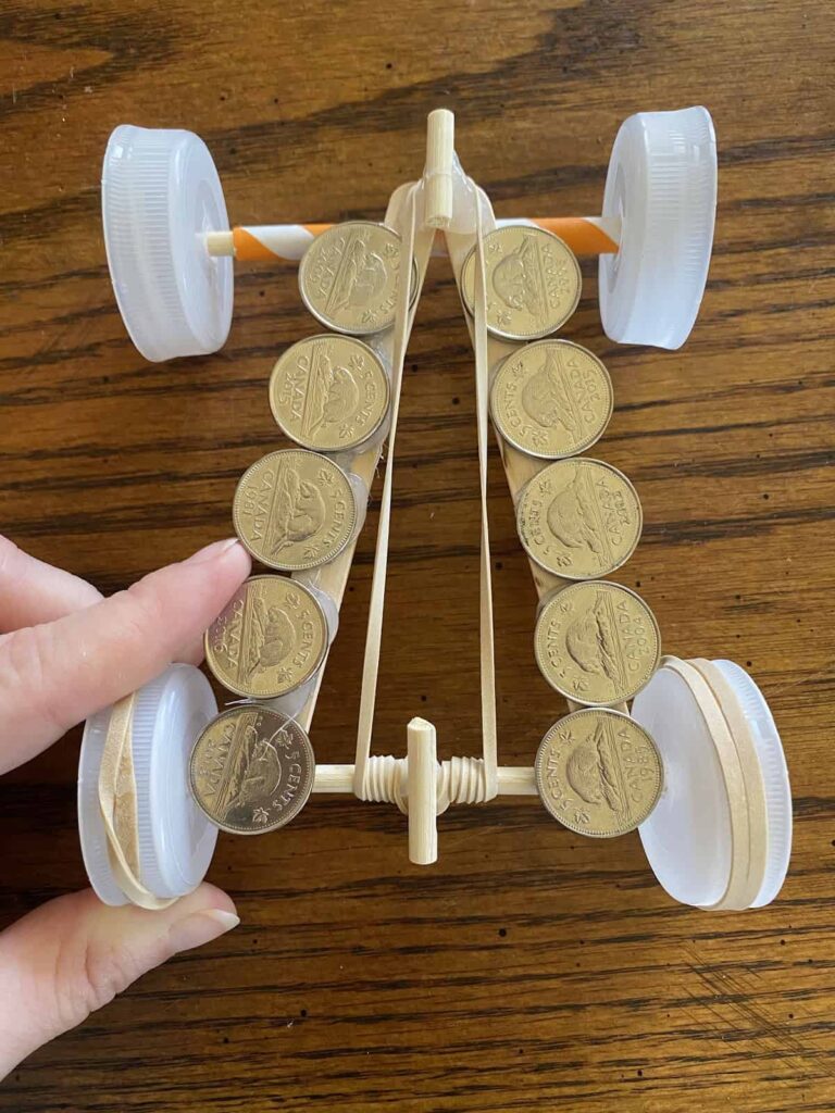 Coins laying on top of a race car made from popsicle sticks, straws, and bottle caps.